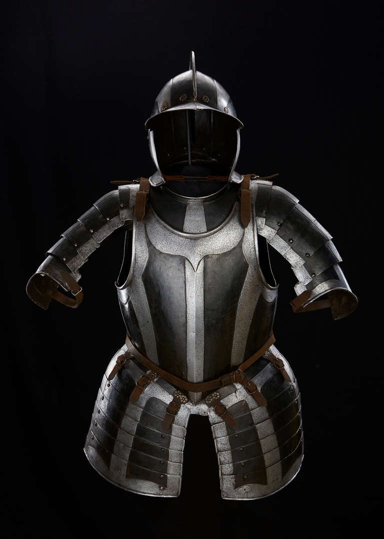 This armour is decorated with blank embossed bands contrasting against a blackened ground. It comprises a burgonet helmet with two cheek pieces, a gorget of two plates hinged with a turning rivet at the right side and closed by a sliding rivet at