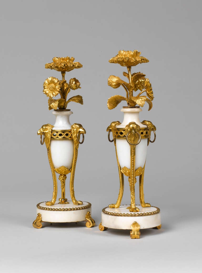 A rare and elegant pair of Louis XVI giltbronze and white marble candlesticks. Each with an ovoid white marble body issuing a floral spray with a flower head nozzle, supported by three curved monopodiae descending from eagle heads, each with a ring