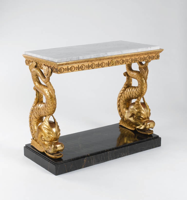 A fine Swedish early 19th century carved giltwood dolphin console table, retaining the original mottled white marble top, the frieze with a central lion mask, acanthus leaves and floral ornaments above two fully carved dolphin supports on a