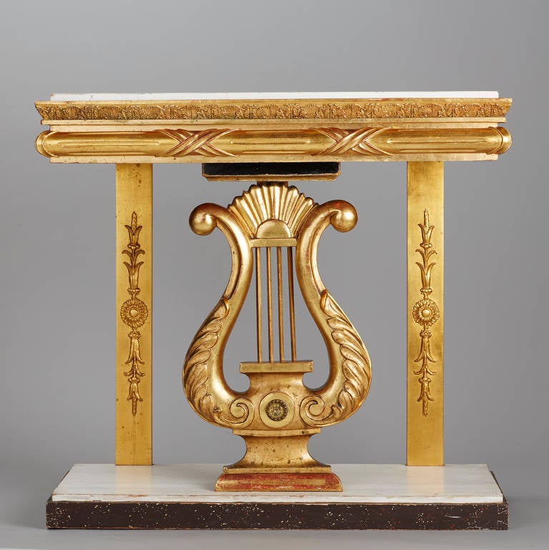 An elegant Gustavian giltwood console table from the early 19th century. The console with inset white marbleized wooden top above a lyre-shaped support and white and faux porphyry painted base. The back with the stamp of the guild from ‘Norrköping.’