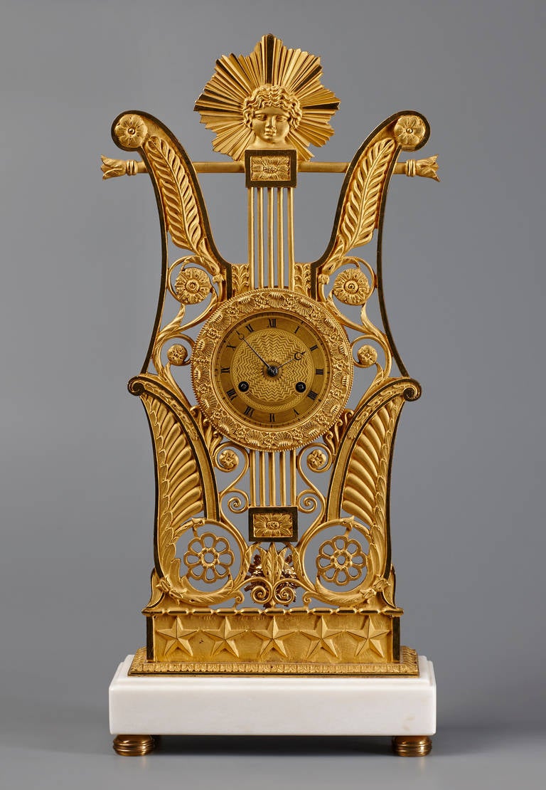Une horloge de cheminée inhabituelle en bronze doré de la période de la Restauration française. Le boîtier en bronze doré, finement percé, a la forme d'une lyre, avec un masque d'Apollon en crête, sur une base à gradins en marbre blanc. Dorure