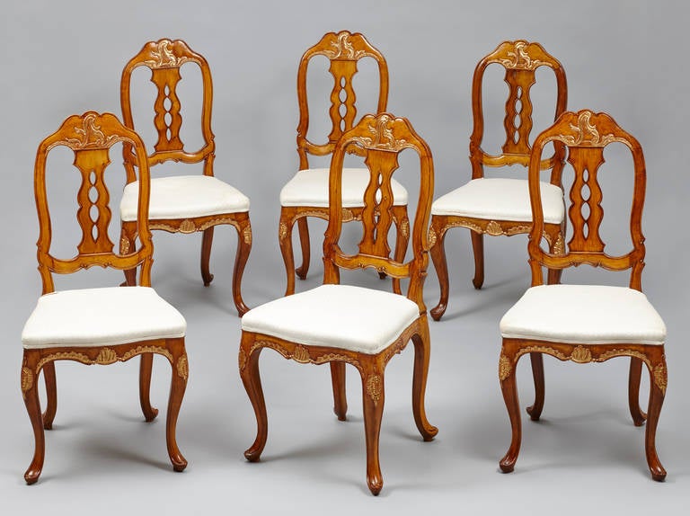 A set of six North European (Danish or North Germany) parcel gilt beechwood dining chairs. The pierced back with shaped splat, above a bow-fronted padded seat, on cabriole legs. Seat rail, legs and top of the back with decorative foliage parcel gilt