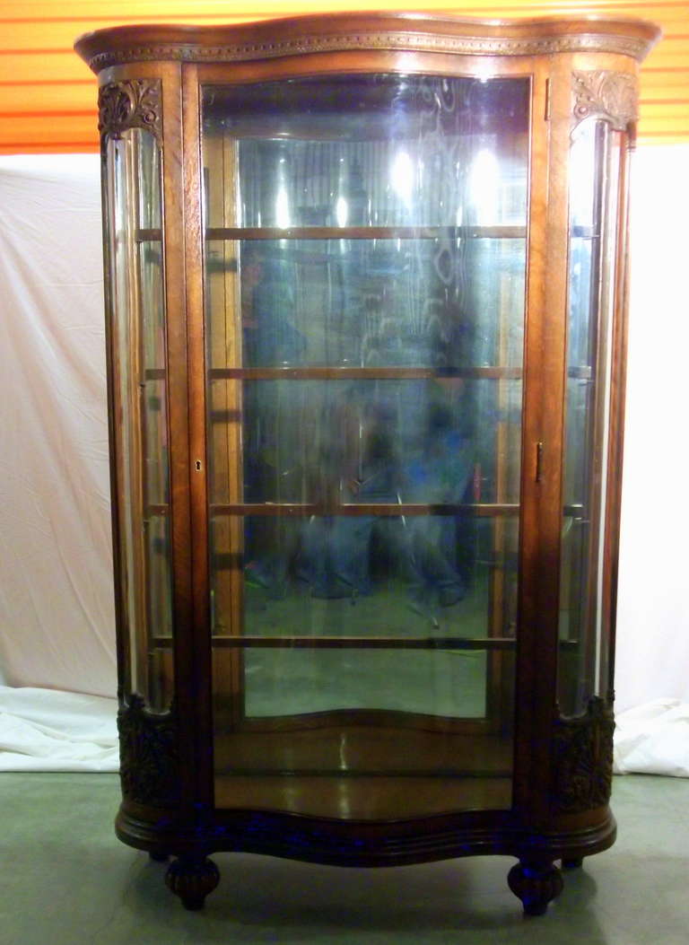 Oak frame display cabinet with serpentine glass front door and bowed sides.  Carved panels, cornices and melon feet.