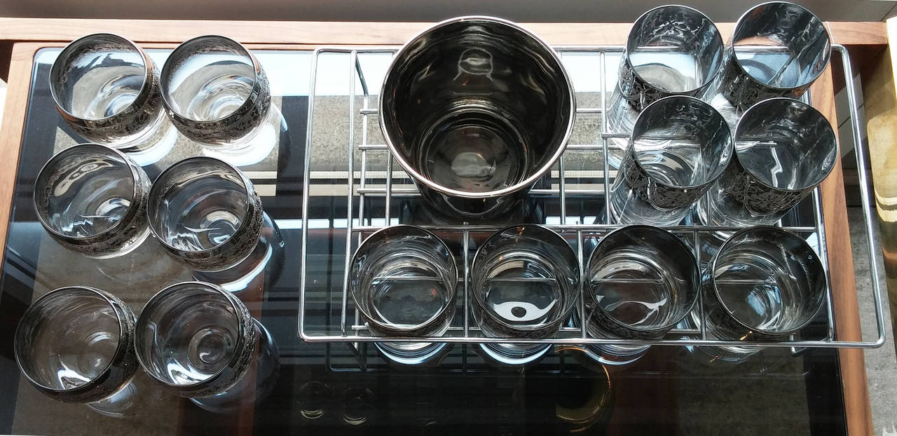 Dorothy Thorpe style set of glasses and ice buckets. Silver rimmed with etched design, there are four highball, four low ball, six rounded low ball and an ice bucket. Included is a holder for part of the set.