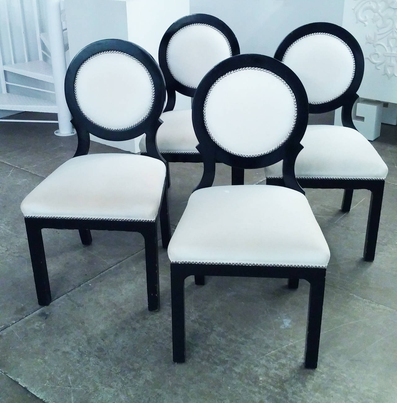 Set of 4 Hollywood Regency style circle back dining chairs. Black lacquered wood chairs with off white upholstery and nickle nail head trim. Lacquer and fabric is in well worn condition. Price is per chair