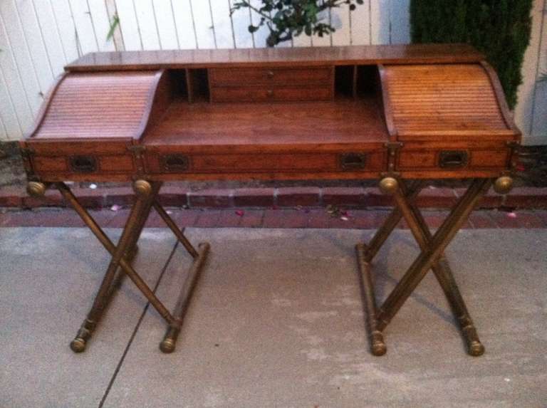 Mid century desk with two roll tops on the sides and three front drawers. Sits on two wooden X bases.  Brass Hardware.
