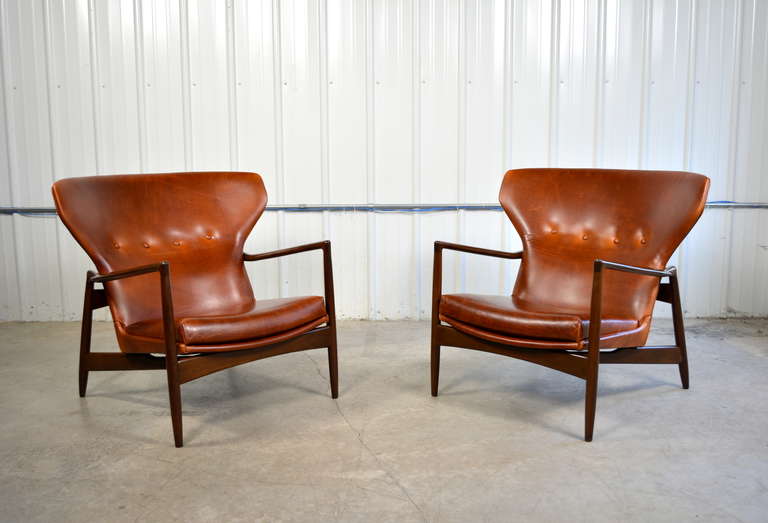 A stunning pair of leather wingback chairs designed by Ib Kofod-Larsen.  Sculptural walnut frames.