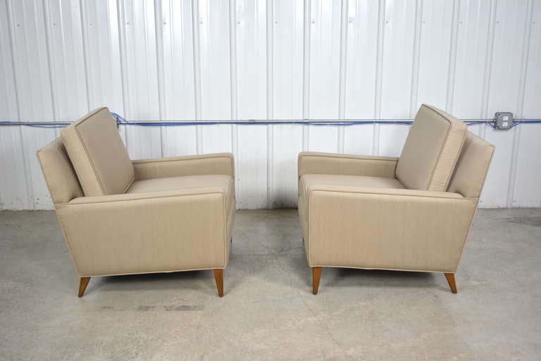 A pair of lounge chairs designed by Paul McCobb.  Elegant Mid Century Modern style.  Solid walnut legs.  Removable seat and back cushions.  Newly recovered in a neutral wool fabric.