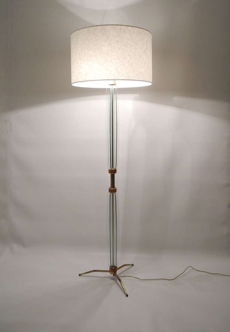 A fine floor lamp with the typical form language of the Fontana Arte house. The brass stand with three glass columns is arranged in the shape of a star and is held by maple rings. The cylindrical shade is a contemporary reproduction.