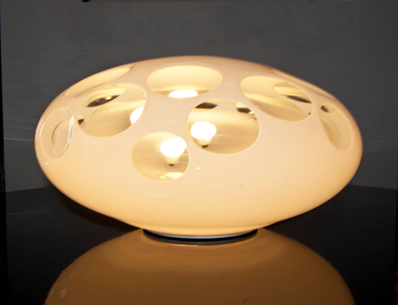 Oval-shaped table lamp in lattimo-glass with transparent lenses which gives a pleasant light and atmosphere.