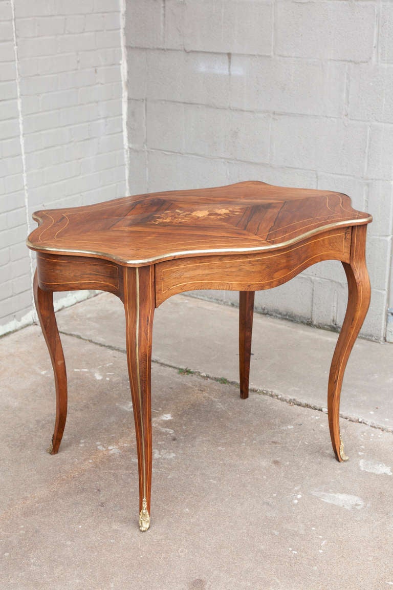 The very rare shape of this nineteenth century Louis XV style writing table makes it a stand out.  The surface is inlaid rosewood and lemonwood marquetry, with bronze detailing around its top edge. This desk has sleek Bombé curves and elegantly