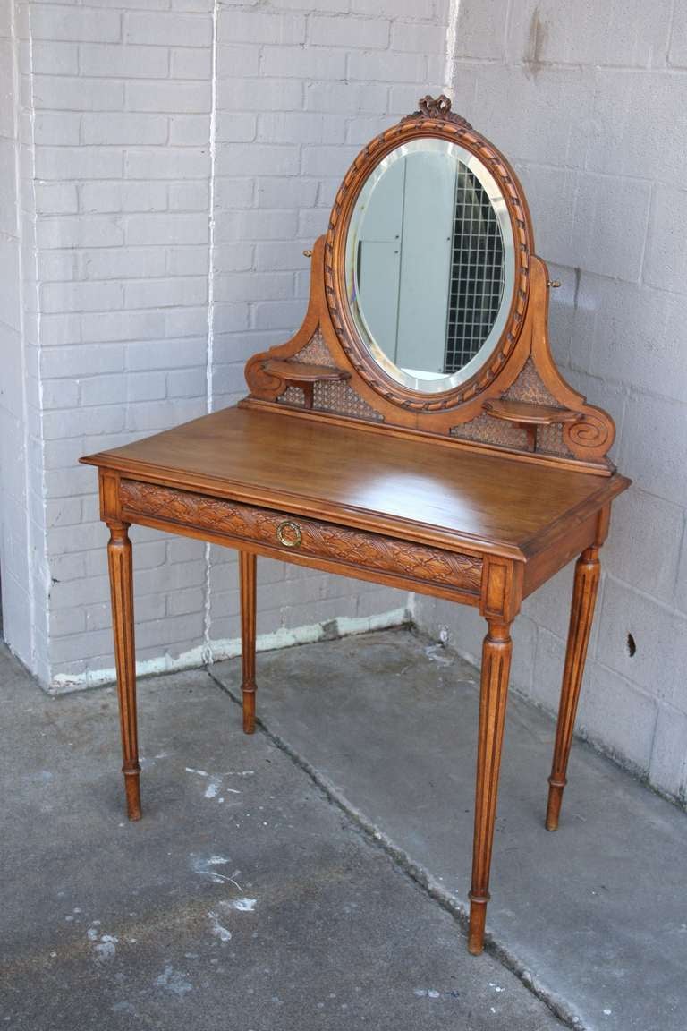 This Louis XVI style walnut vanity table is finely detailed; with bronze accents, delicate carving, caning, and a beveled mirror.  Although this is a great piece for a ladies dressing space, it would also work well as a desk.