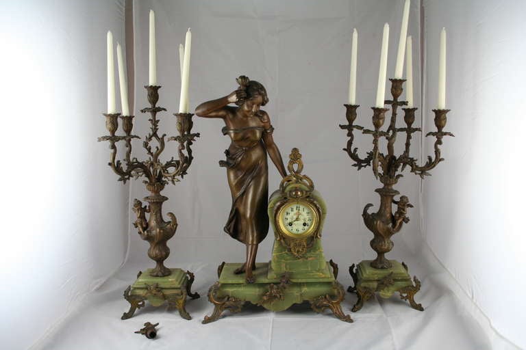 This stunning Art Nouveau Garniture De Cheminée (mantle piece ornament) is a rare complete find; with clock, candelabras, and original snuffers. The patinated bronze regule figure of a woman with a tulip is on a light olive green onyx base. The
