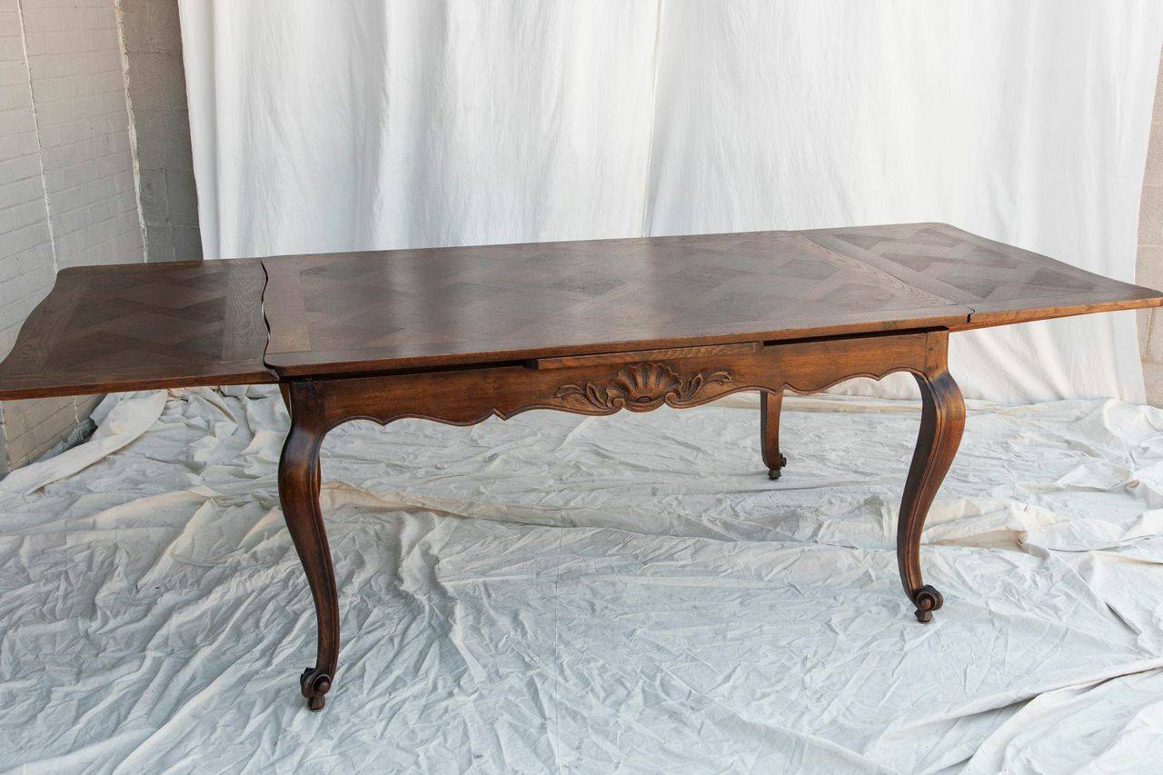 This hand carved oak Louis XV style draw leaf table features a  parquet top and a double beveled edge.  The carved shell motif and classic escargot feet give this table a classic French feel.  The leaves, at 19