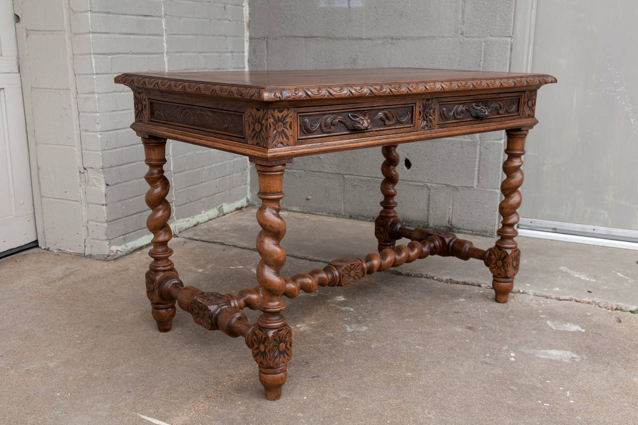 This elaborately hand-carved oak Louis XIII writing table features barley twist legs, gargoyle drawer handles and a carved center stretcher for excellent stability. This small-scale desk has a large-scale presence and with carvings on all four sides