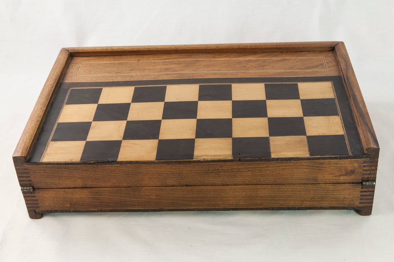 An artisan-made c. 1900 game board and box, this piece is meant for checkers, chess, or backgammon.  Complete with hand carved wooden chess pieces, a complete set of wooden checkers, and a pair of wooden dice, this large game surface closes to make