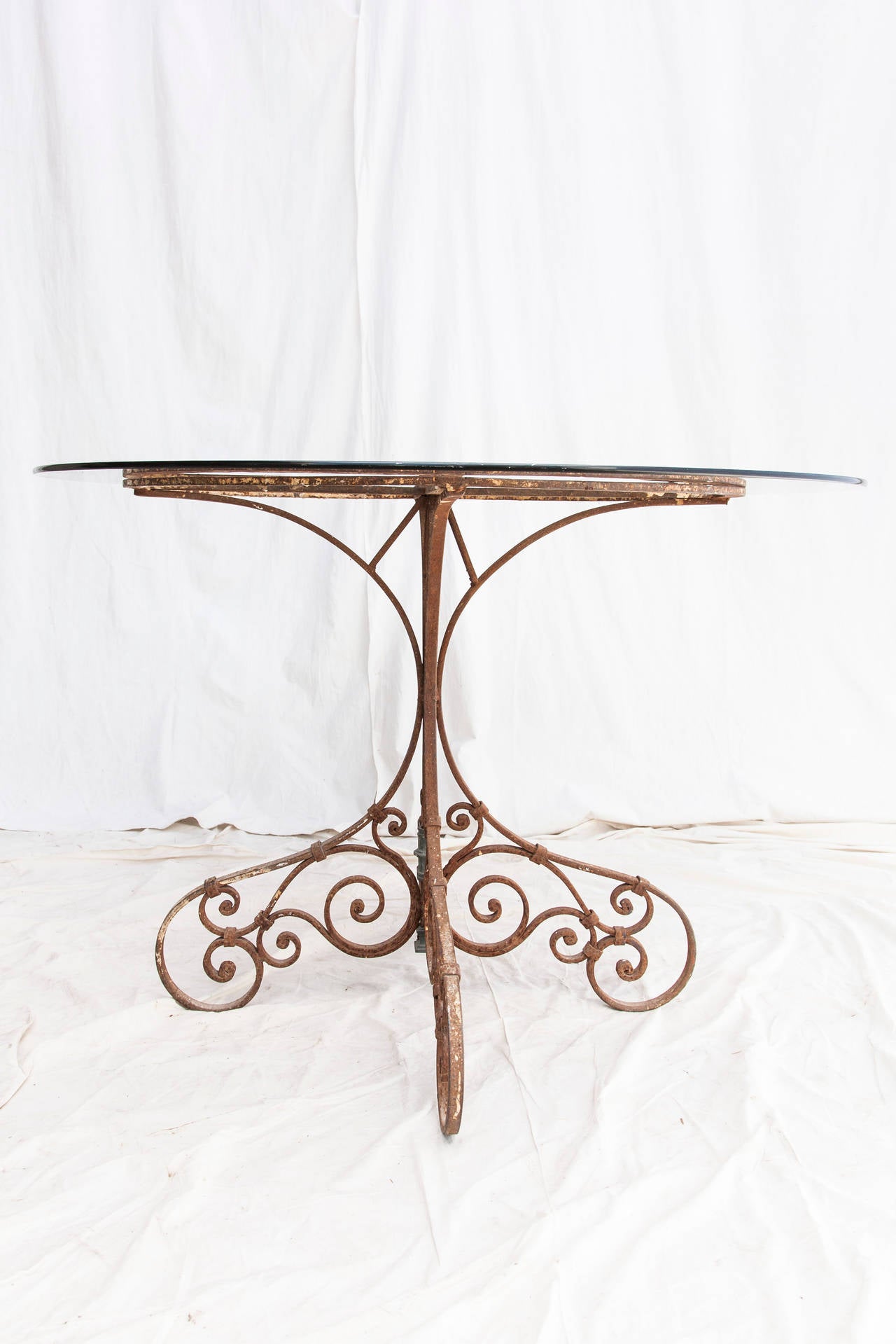 This late 19th century hand-forged iron table base has acquired a beautiful rustic patina. The smoked glass is very forgiving for outdoor dining, while the elegance of the hand-forged curvature in the base makes this table a great fit for an entry