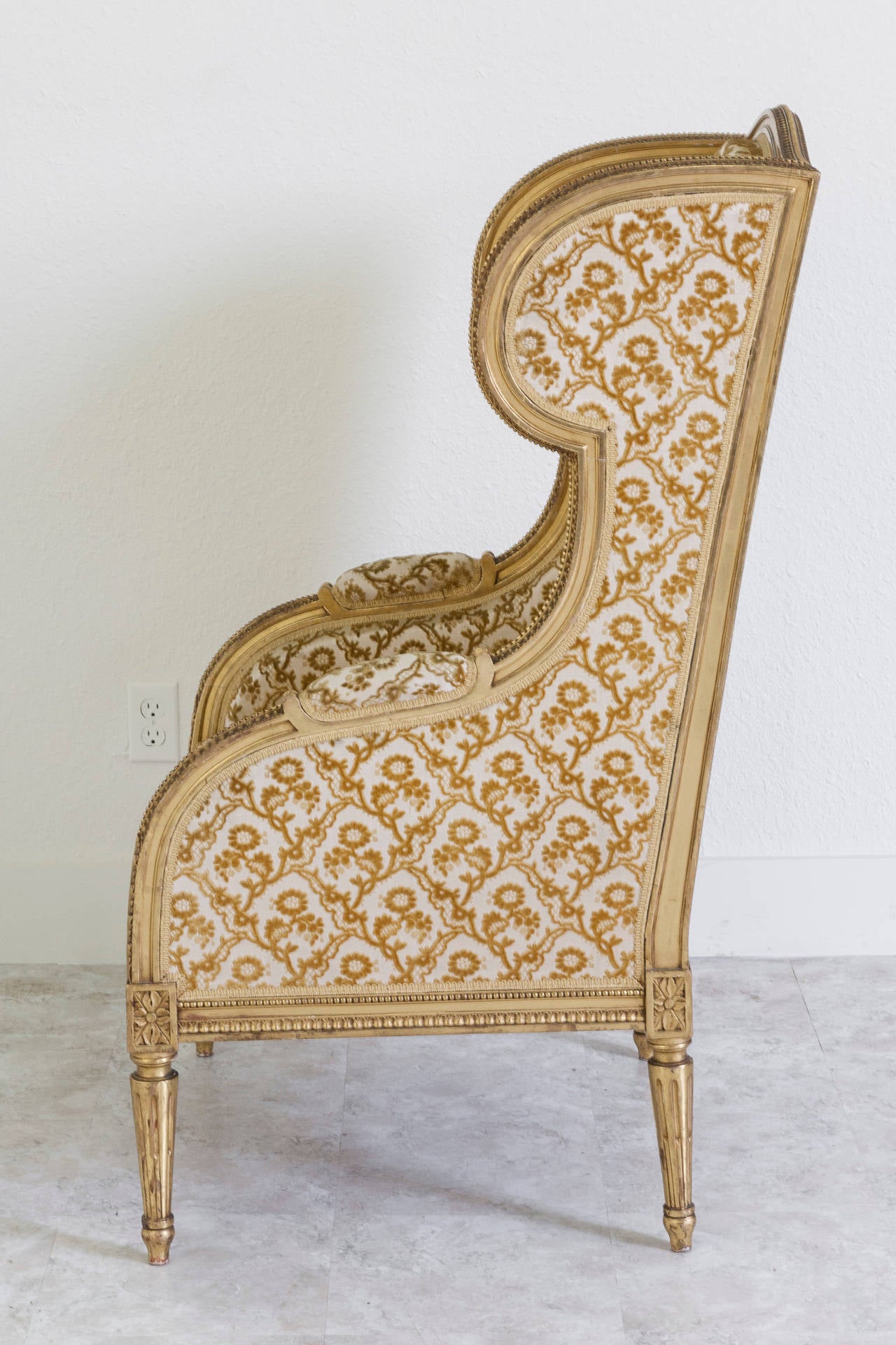 This Classic Louis XVI style wingback chair has been gilded with 22-karat gold leaf and upholstered in a rich gold and ivory mohair. The effect takes this classically quiet Silhouette and transforms it into a style statement piece. In excellent