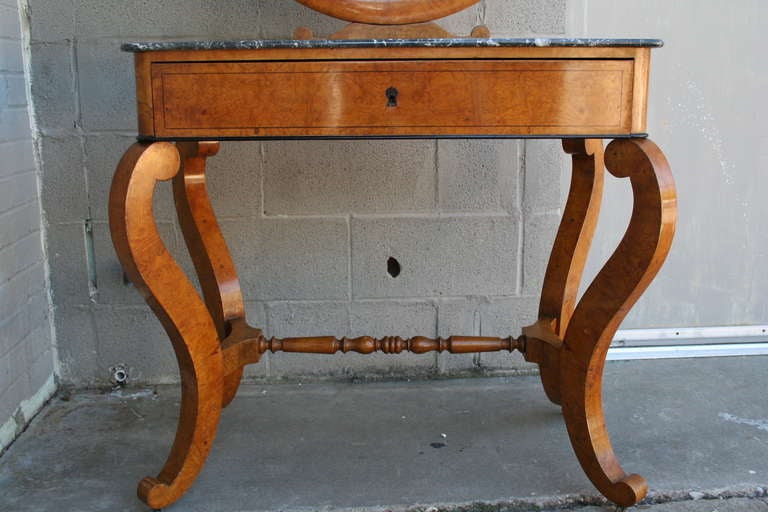 Charles X burled elm vanity table with cabriole legs and turned stretcher, circa 1820. Its single drawer has divided compartments, and its swivel mirror is supported by two swans. The original Saint Anne marble top has a routed border to keep