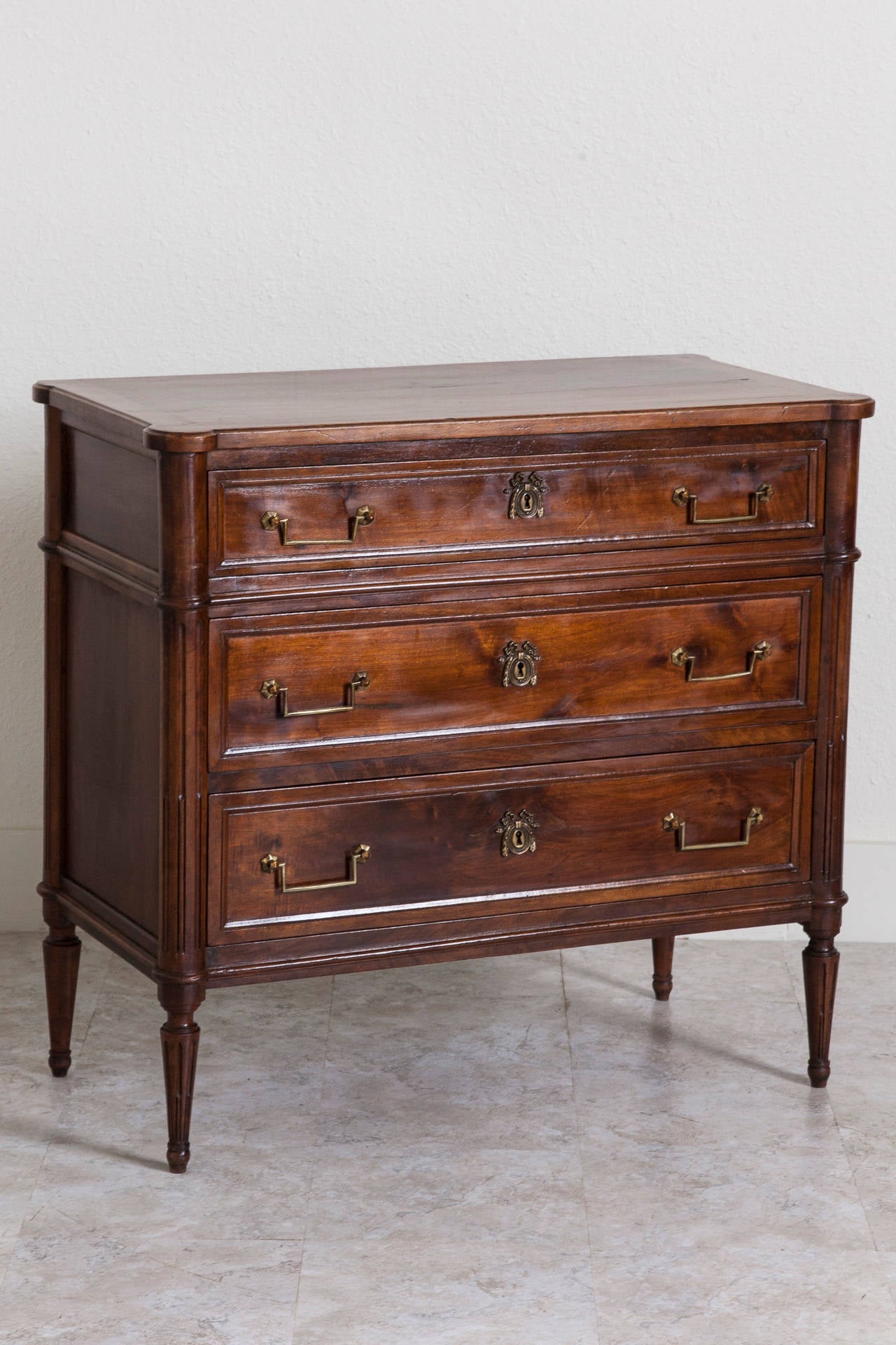 This 19th century Louis XVI style commode or chest of drawers is made of solid French walnut and features three drawers with original bronze hardware. Its fluted sides extend to tapered hand-turned legs. Created in the 1880s and used in a Paris