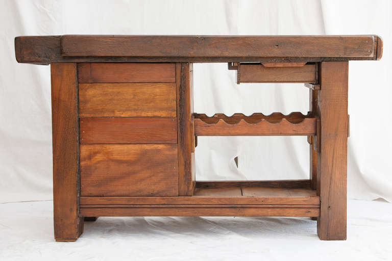 This nineteenth century artisan made workbench from Normandy, France features a four inch thick top and a slot at the back originally used to hold saws.  Its closed cabinet, single drawer, and wine rack make it a practical piece to use as a wine