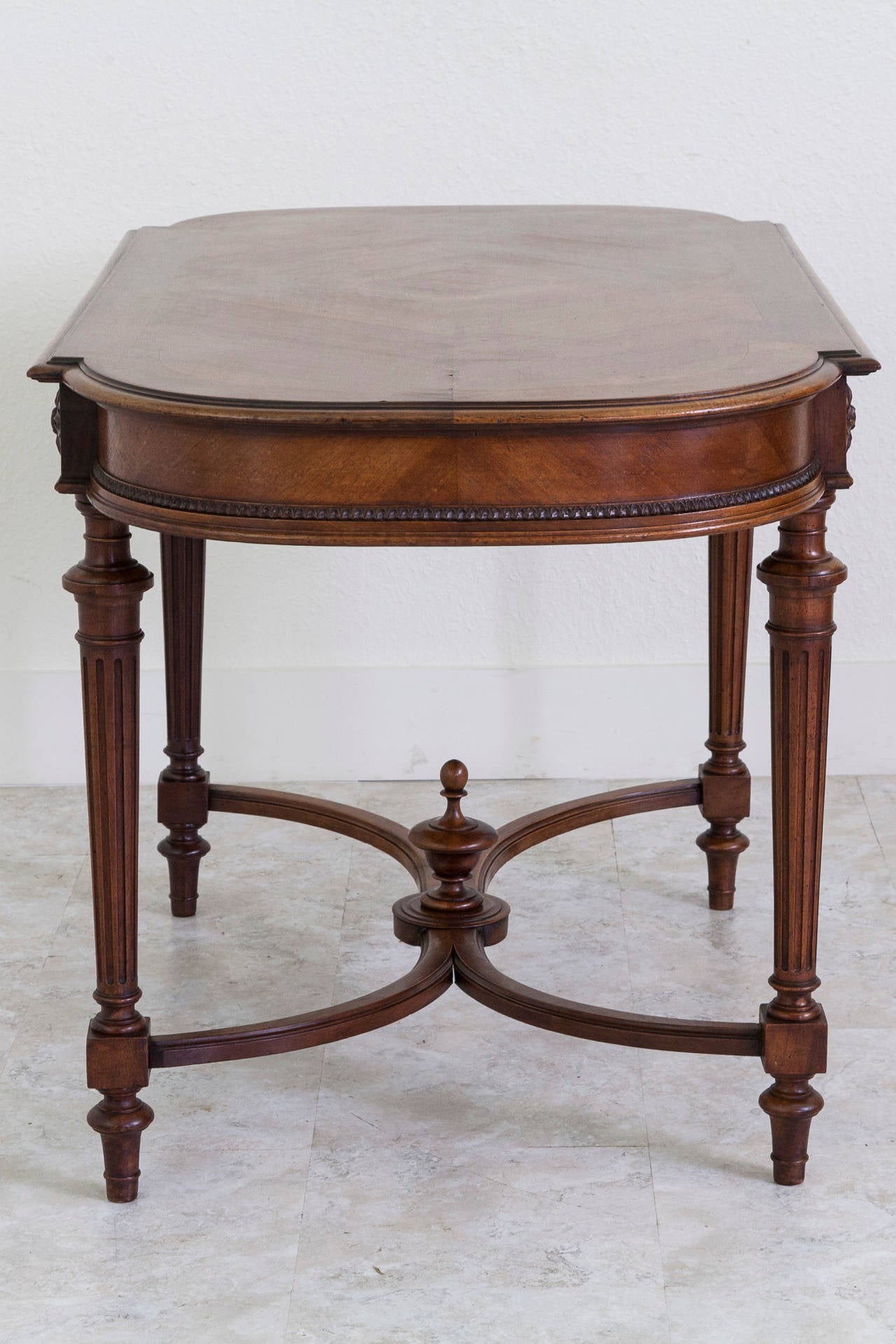 An elegant geometric diamond pattern created from bookmatched walnut gives the top of this desk great interest. Its simple carved apron allows the walnut wood grain to shine, and features a single wide hidden drawer. Rosettes on each side lead to