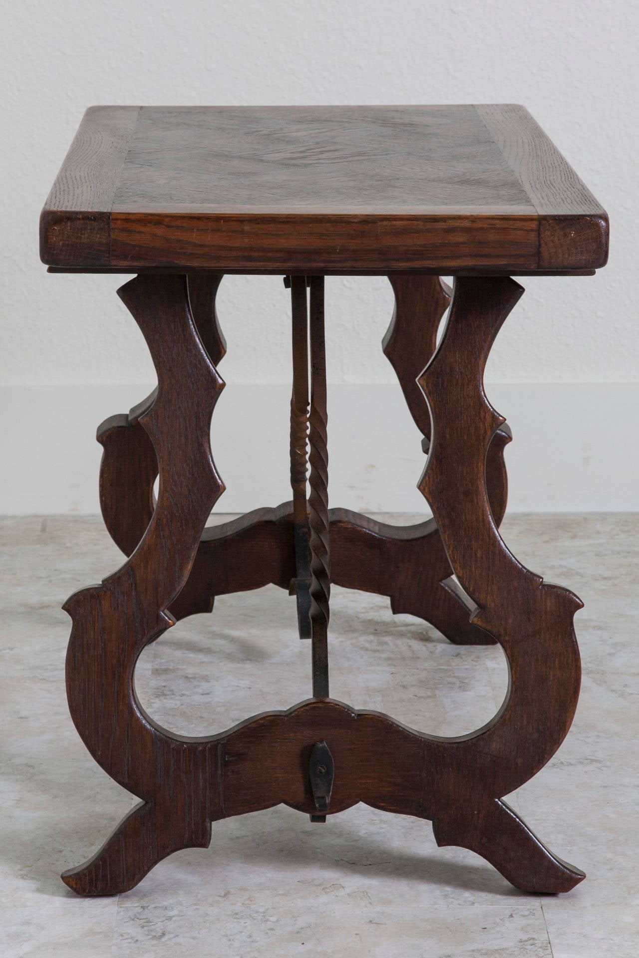 This handsome little coffee table has been constructed in the manner of a large Spanish Renaissance table. The hand-forged iron stretchers, parquet top, and elegantly carved legs give this small piece a large presence. The scale of this table would