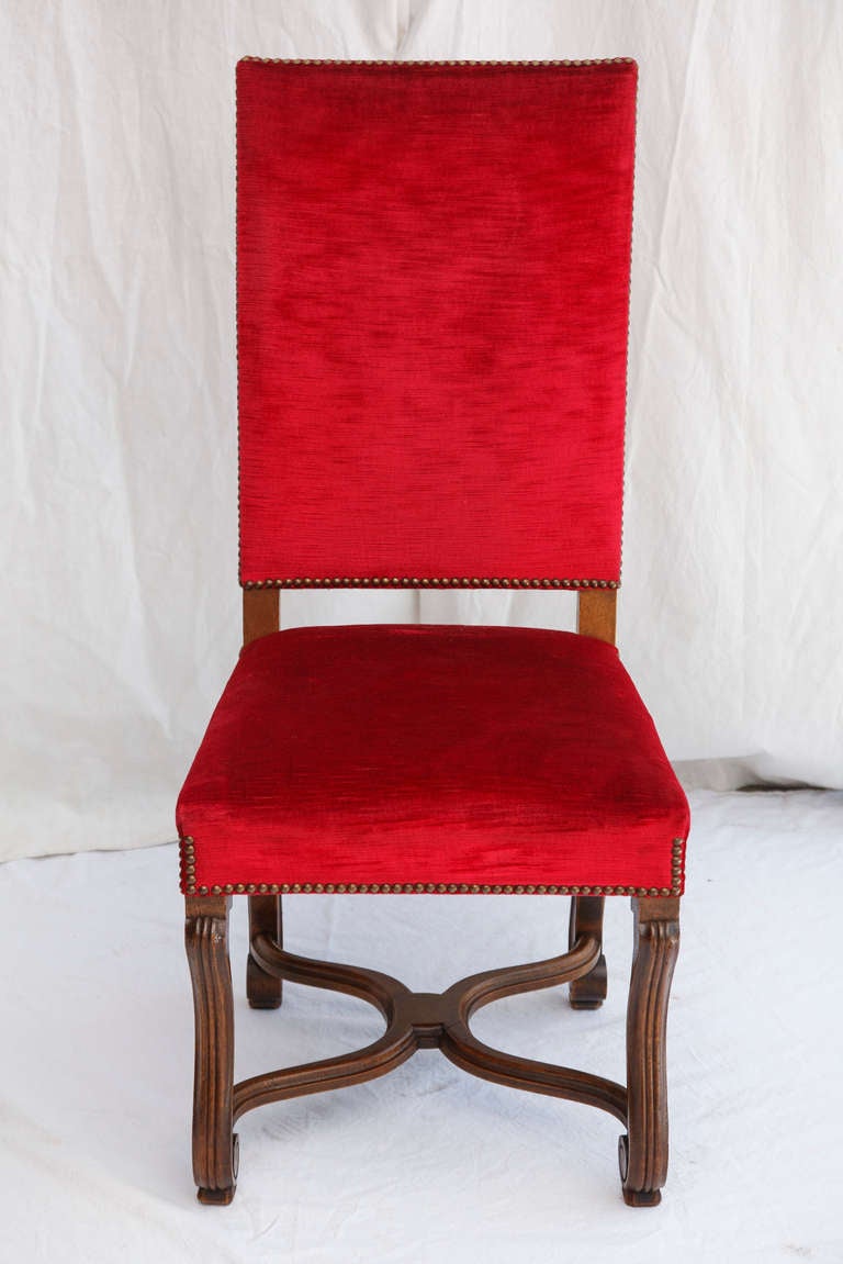 Set of four hand carved oak Louis XIV style fluted mutton leg side chairs with X stretcher upholstered in red velvet with nail head trim.  C. 1900.