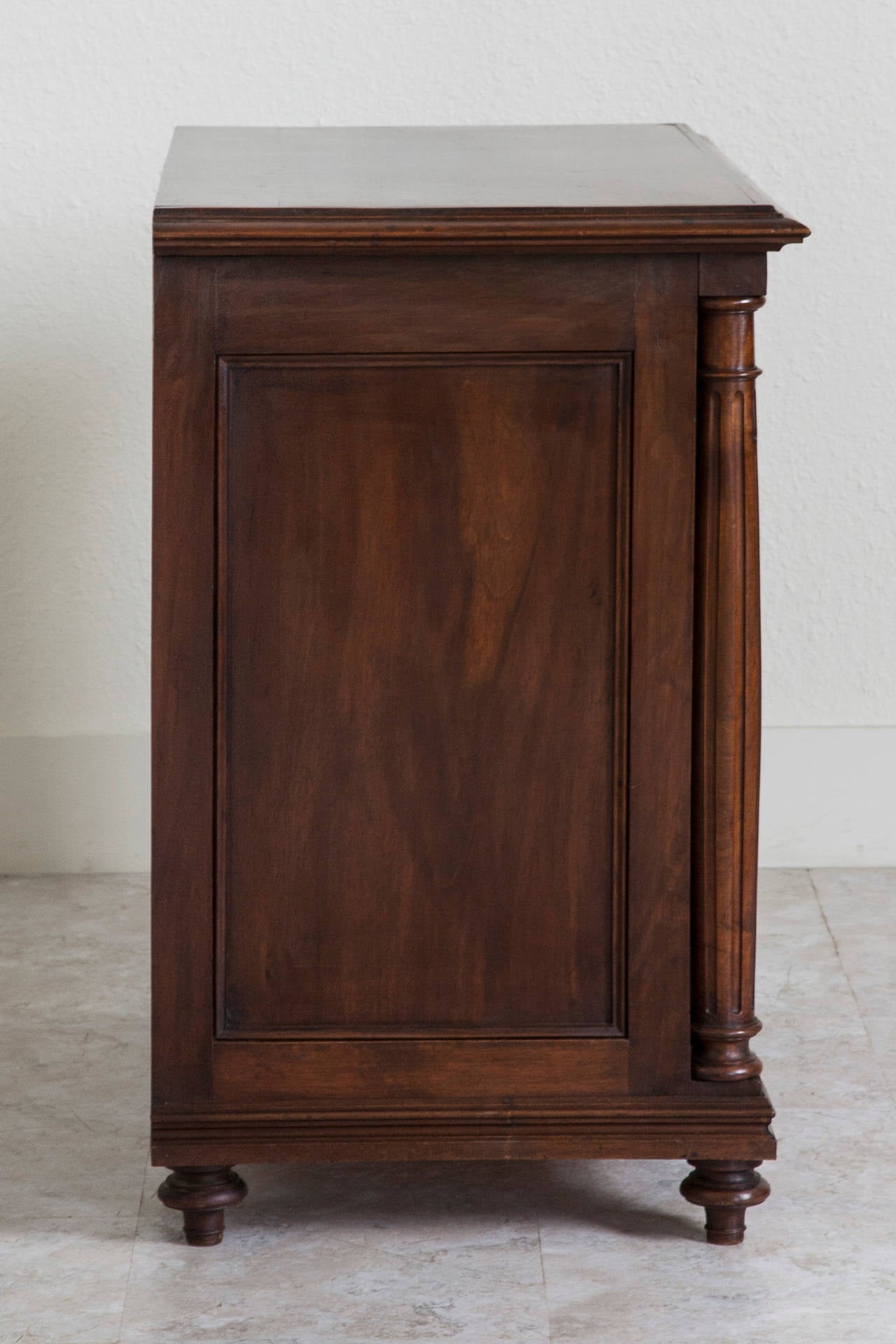 This handsome small-scale walnut chest features four locking drawers flanked by fluted columns. Its simple lines allow it to mix with a variety of interiors, and its smaller size makes it ideal for use beside a bed or in a small entryway. Found in