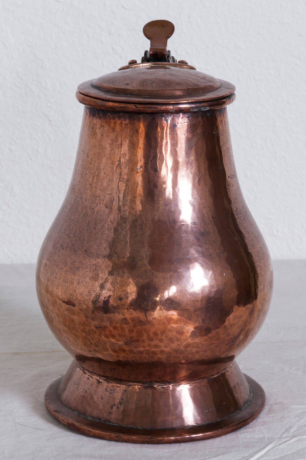 This large 18th century hand-hammered copper tankard from France features visible seams where the copper smith made his joinery in fashioning this one-of-a-kind piece. Both handle and hinged lid have copper rivets. Weighs 10.5 pounds.