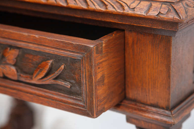 This hand carved French Oak Louis XIII style writing table has a wide single drawer and gold tooled leather top, circa 1880. The carving, which features barley twist legs and oak leaf motif, is continued on all sides.