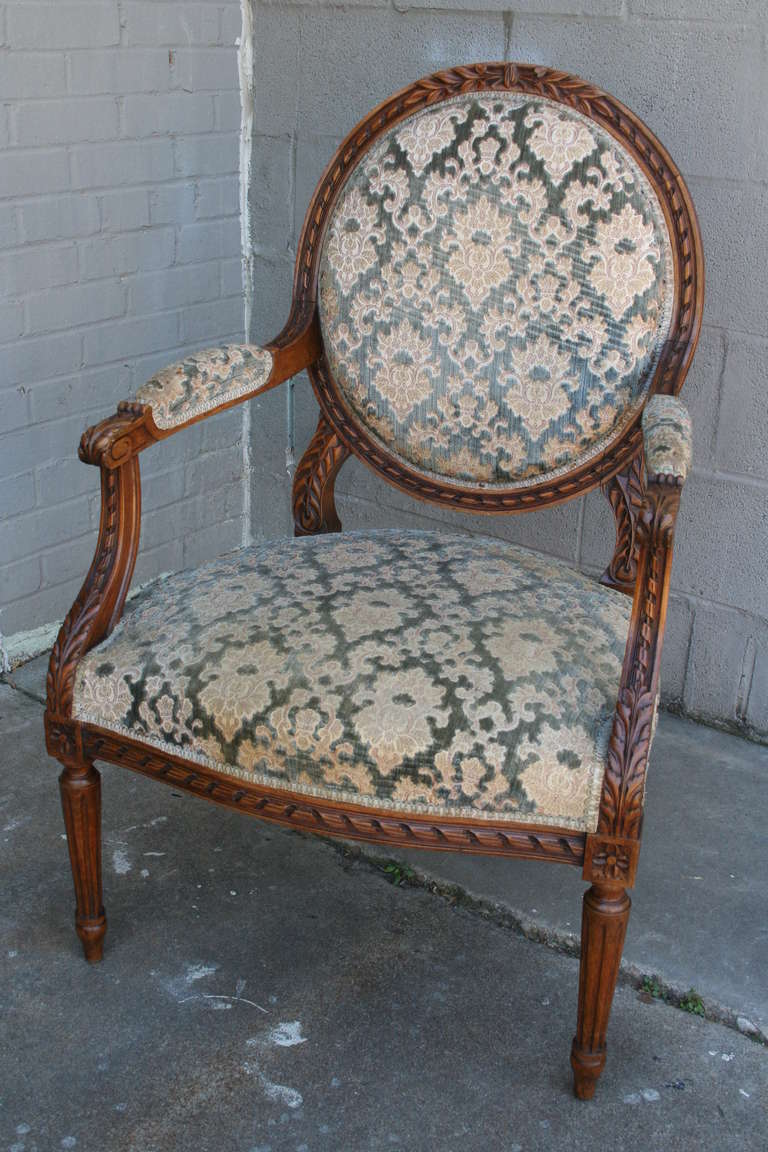 This pair of nineteenth century Louis XVI style medallion back armchairs feature hand carved acanthus leaf and ribbon detailing and fluted legs.   Upholstered in cut velvet with nail head trim, their classic appeal and sturdy construction will