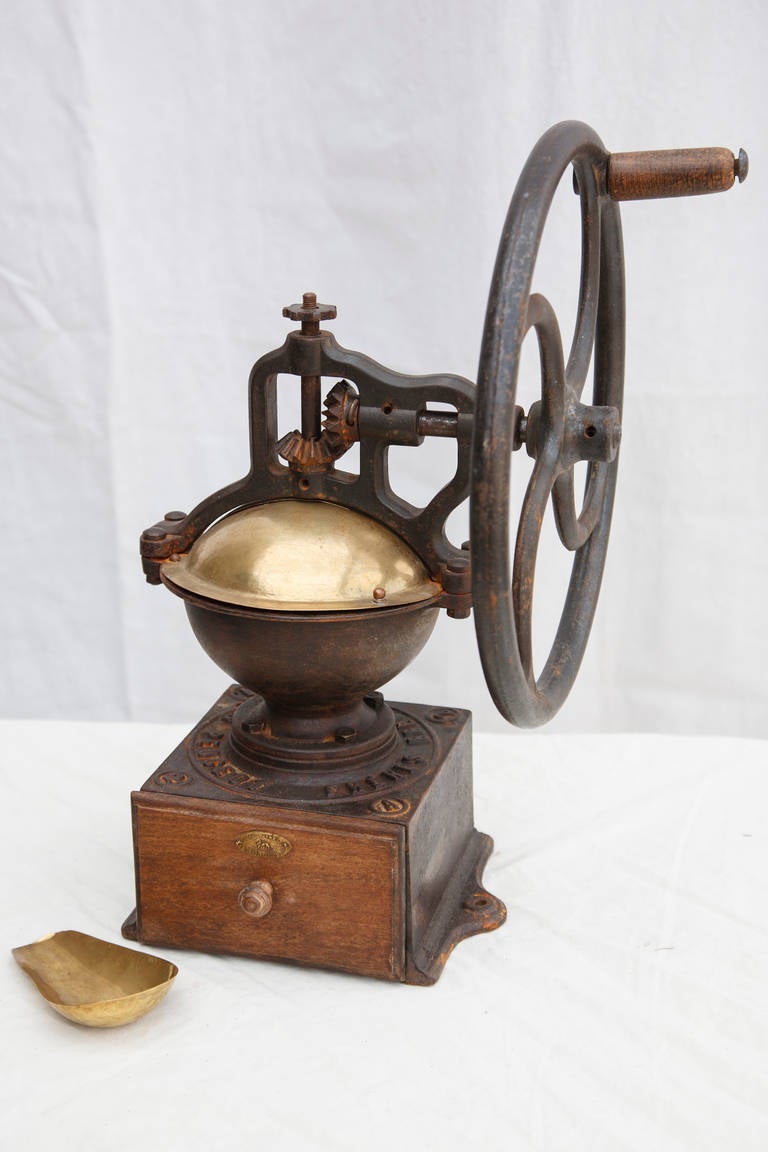 This large iron coffee grinder from a French bistro is marked by its maker, Peugeot Frères, both on its ironwork and on its small brass seal.  The brass top swivels out to receive coffee beans for grinding.  Ground coffee drops into a wooden drawer