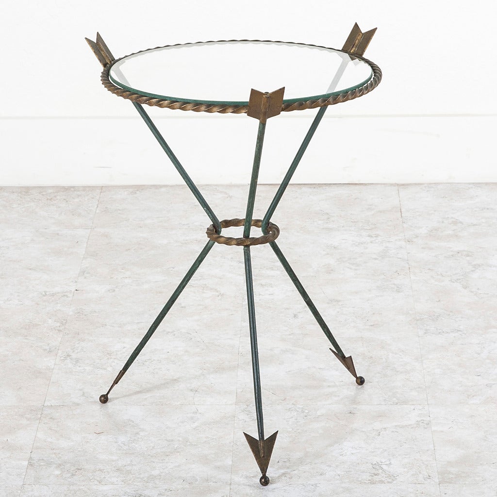 Finished in lovely green and brass tones, this iron side table features the classic Directoire arrow motif. Accented with elegantly turned circlets in a rope motif and ball feet, this versatile piece will create interest in any space. Glass top.