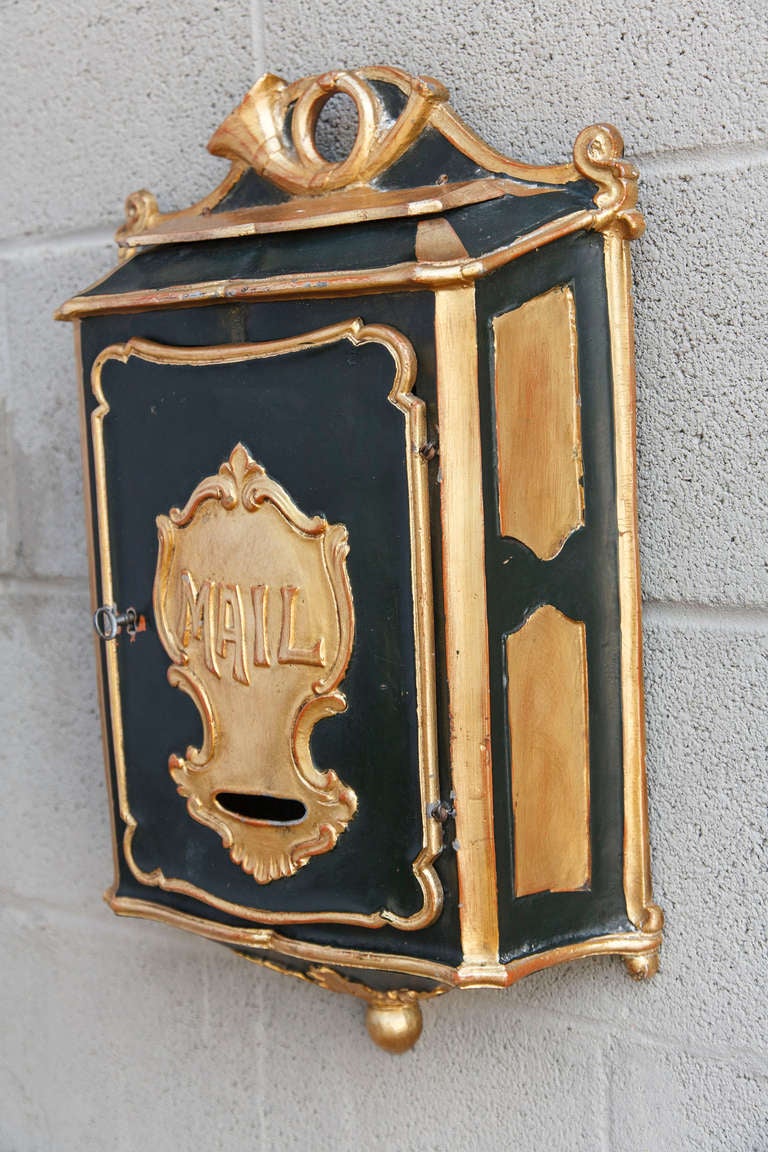 Black and gold painted Art Nouveau cast iron mailbox with lid that lifts at the top to reveal mail slot and door that unlocks with original key to retrieve mail.
