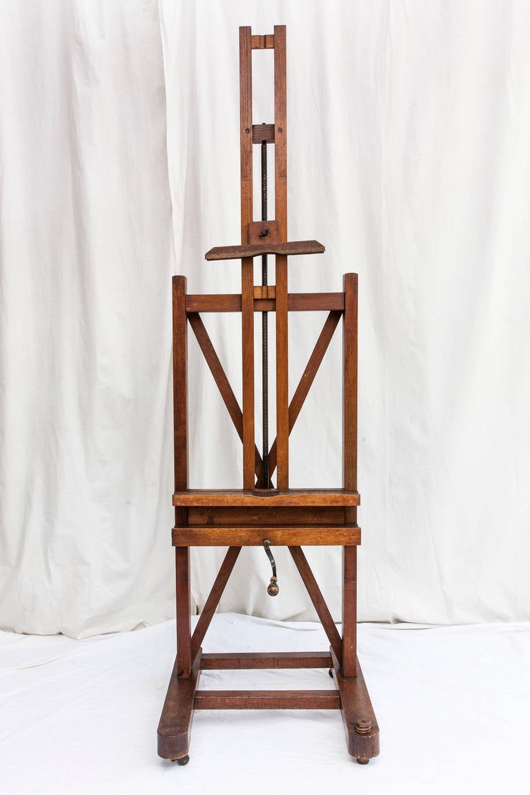 This late 19th century oak artist's easel has its original functioning crank mechanism to adjust the tray height.  Purposely created with three castors, its fourth foot is a wooden screw which keeps the easel in place during the artist's work when