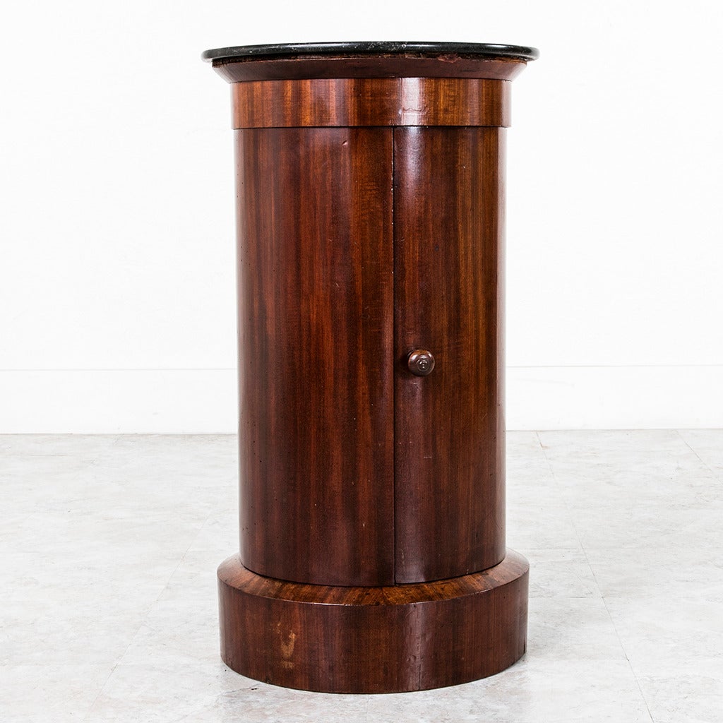 This handsome French Empire period mahogany somneau or drum table features its original black marble top and two interior shelves. The simple cylinder design of this piece allows its beautifully French polished mahogany to shine. This Classic piece