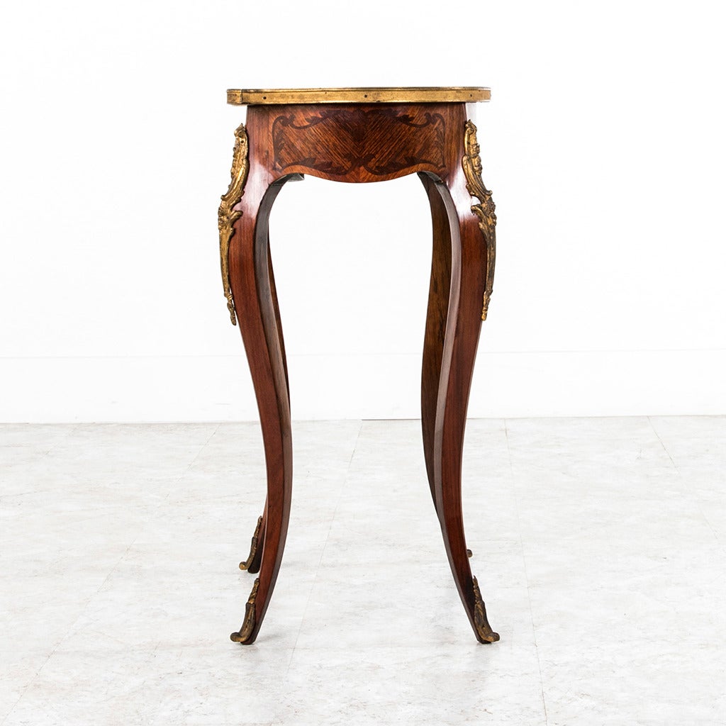 This 19th century Louis XV style marquetry kidney table features intricate inlay with a central bouquet of lilies on its top. A bronze band surrounds the surface and gilt bronze ormolu graces each cabriole leg ending in bronze sabots. With a single