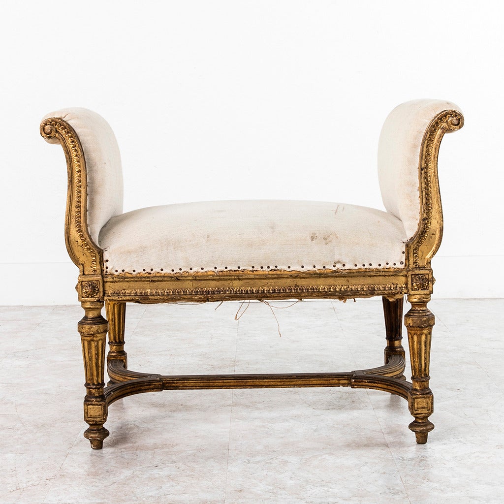 This beautifully aged giltwood banquette features high curved arms and simple linen upholstery. The unusually sturdy construction of this piece along with its elegant and Classic Louis XVI lines will make it a versatile and lasting piece for any