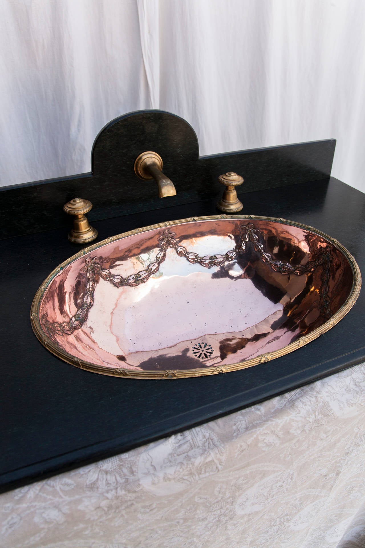This exquisite one-of-a-kind Louis XVI style copper and brass sink features its original bronze faucet and handles. The sink and bronze handles have a matching Louis XVI festooned garland and ribbon motif. Mounted in its custom black marble counter