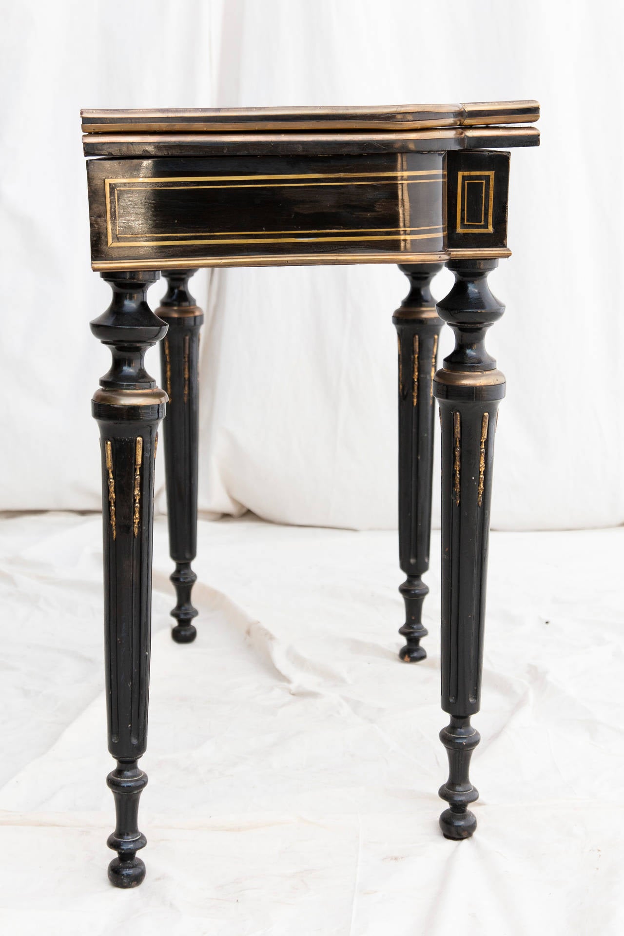 This elegant Napoleon III period black lacquer console table features a musically themed bronze inlay, bronze banding, and ormolu accented fluting. The top swivels and unfolds to reveal a 34