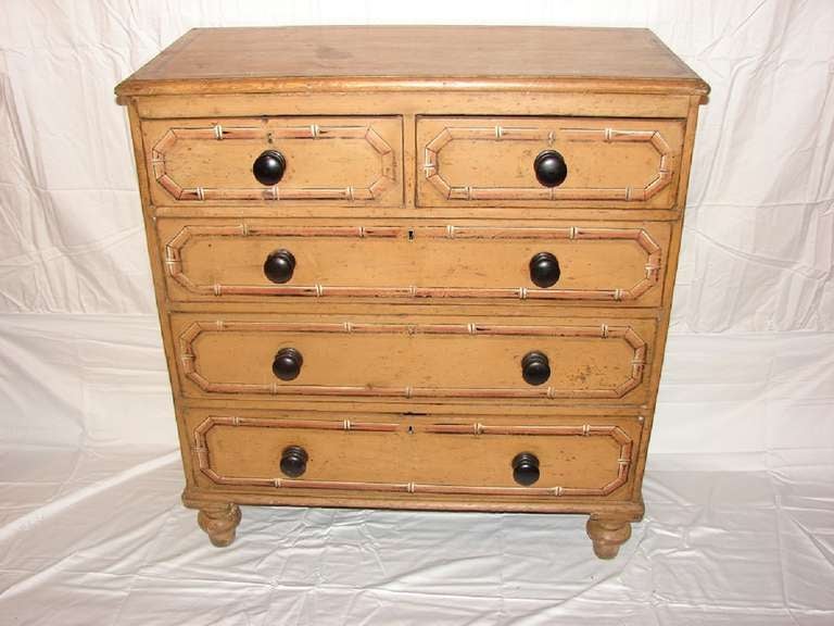 Pine chest of drawers with its original mustard color paint. Painted faux bamboo decoration forms panels on the five-drawer fronts as well as on the top and sides of the chest. Contrasting round ebonized wood pulls. Turned feet.