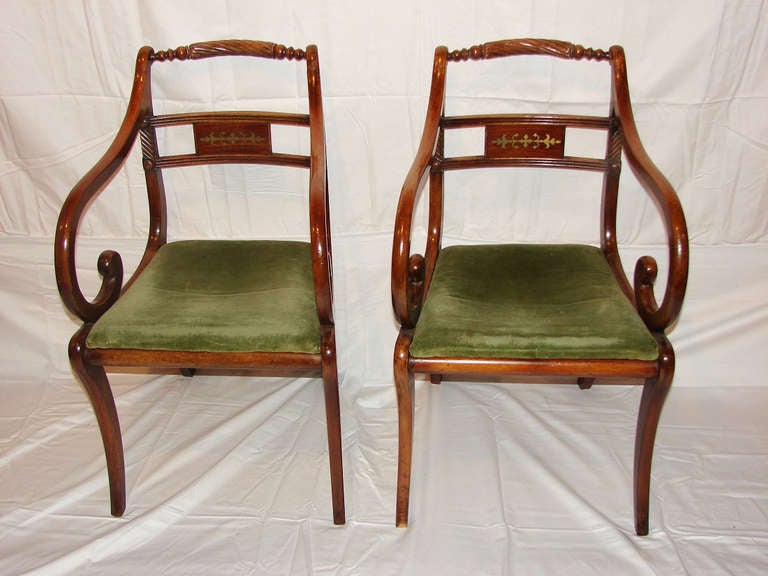 Elegantly curved scroll arms and saber legs add to the appeal of this attractive pair of mahogany armchairs. The crest rails are turned with insets of a carved, twisted rope motif. The reeded splats
have a rectangular center panel with brass inlay