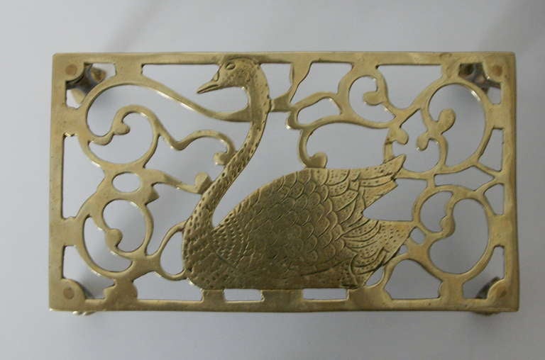 The top of this brass trivet features a lovely swan with incised feathers. The pierced curvilinear background echoes the graceful curves of the swan. Four legs with ball and claw feet support the trivet. Underside appears to be stamped R D 729088.