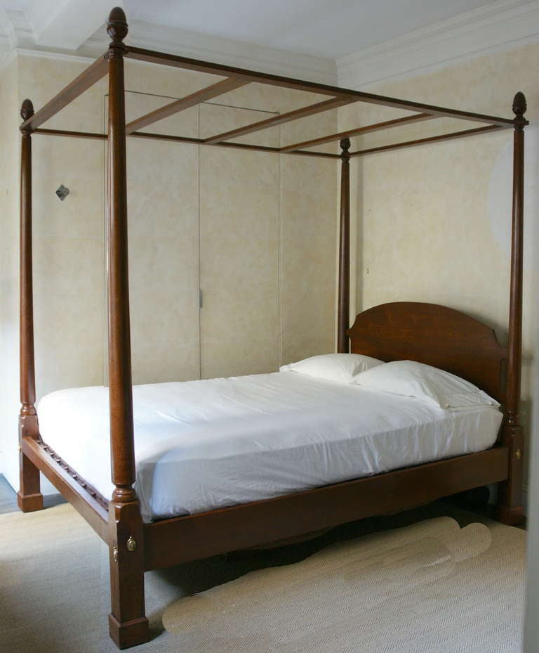 Walnut tall post bed with simple arched headboard and slender round tapering posts terminating in acorn finials. The posts rest on carved block legs with brass hardware. Plain canopy stretchers and slats. Side rails and foot rail. Note that the