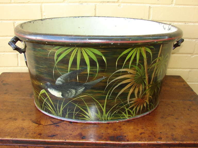 This wonderful tole foot bath is decorated with a bird amid exotic palms. Painted lines of red, one around the top rim and one around the bottom rim, contrast nicely with the striated background of black, brown and green. The bird is rendered in