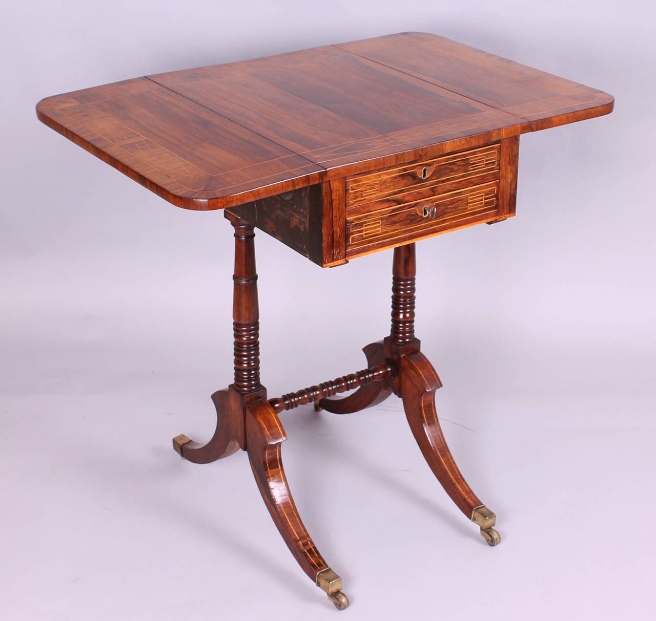Regency period rosewood work/occasional table; the drop-leaf top with finely figured and coloured veneers, double cross-banded and inlaid with boxwood geometric stringing; fitted with two shallow drawers, and corresponding dummies, on turned