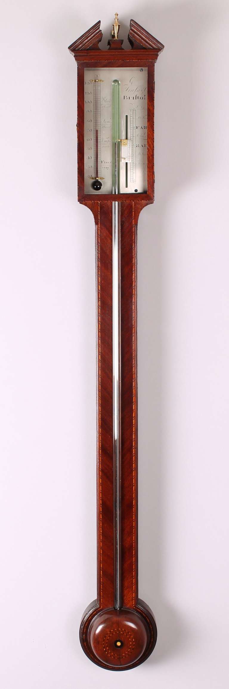 George III mahogany stick barometer by C Trassi & Co, Bristol; the silvered register fitted with an alcohol thermometer behind a glazed door; with a broken moulded pediment and a domed cistern cover with a central paterae and black and white