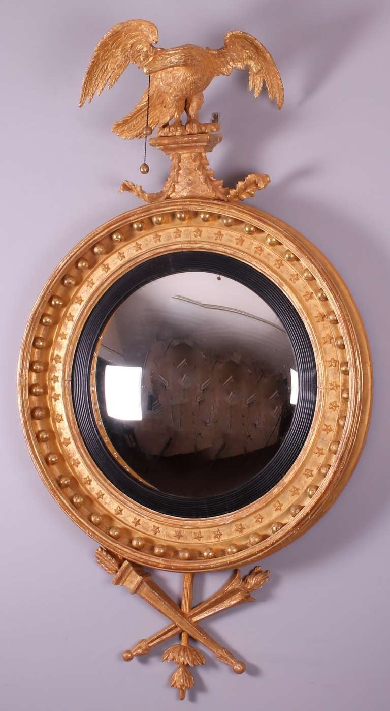 Regency period carved and gilded convex mirror. The 16.5 inches diameter plate contained in a handsome 'Classic' Regency cavetto-moulded frame with ball and star motifs, surmounted by a finely carved eagle cresting and with a crossed quiver and
