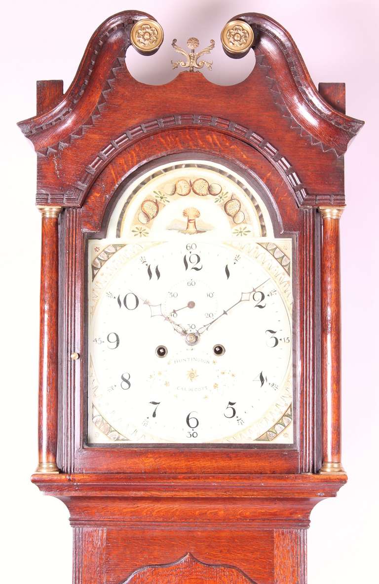 Early nineteenth century oak long-case clock by Caldecott of Huntingdon; the 8-day striking movement with an arched enamel dial painted with gilded stylised shells and a sheaf-of-corn; the richly-coloured case surmounted by a swan's-neck pediment